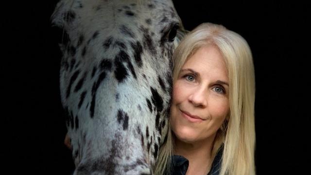 Professor Sandra Swart is pictured next to her horse, which is white with black spots. They are both looking at the camera.